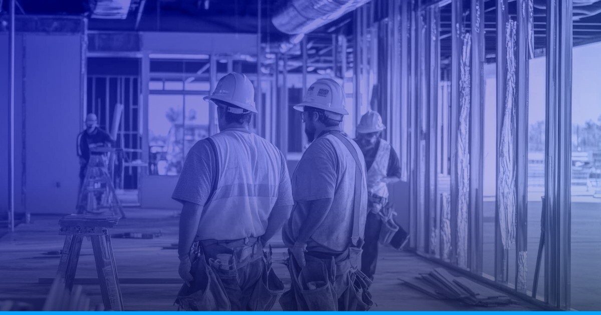 Construction workers in hard hats walking through a commercial retail space under construction, framed with steel studs and exposed ceiling